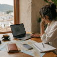 Traveler planning a trip at a cafe table with a laptop, map, notebook, and phone.