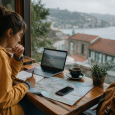 Traveler planning a trip with a laptop, map, notebook, and phone beside a rainy café window