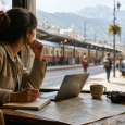 Traveler planning a trip at a café table with a laptop, notebook, and map