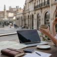 Traveler planning a trip with a laptop, notebook, map, and passport at a café table.