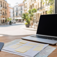 Traveler’s laptop and redacted trip papers on a café table