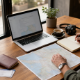 Traveler organizing a trip with a laptop, map, notebook, coffee, and tickets on a café table.